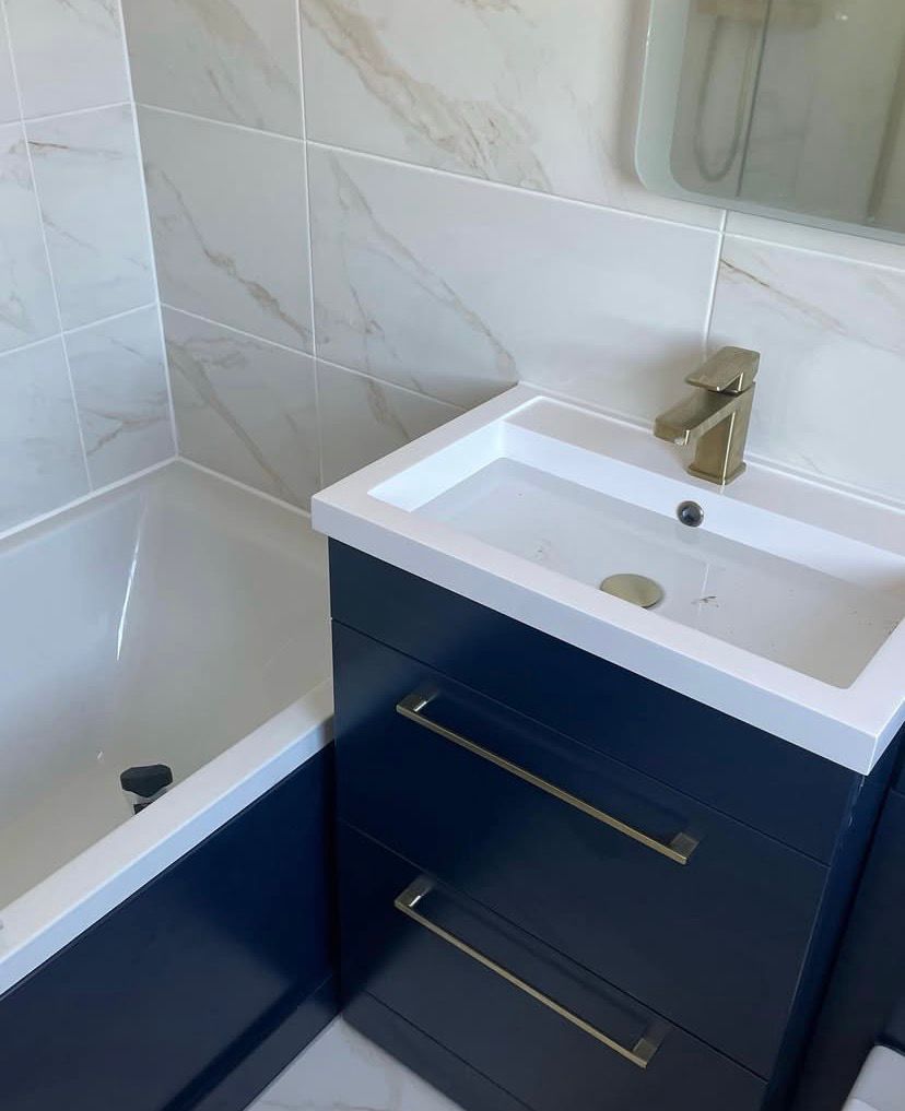 White basin with a brushed brass mixer tap on a navy vanity unit, bath alongside