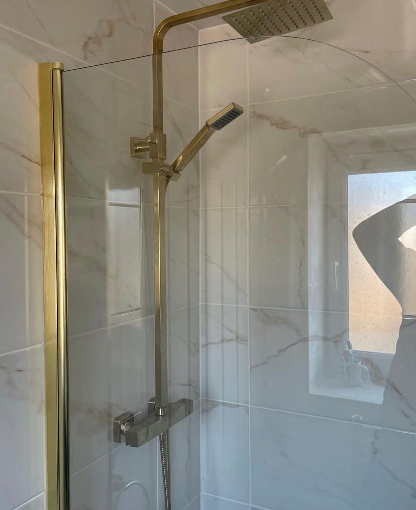 Brushed brass rainfall shower and glass bath screen against marble-effect porcelain tiling