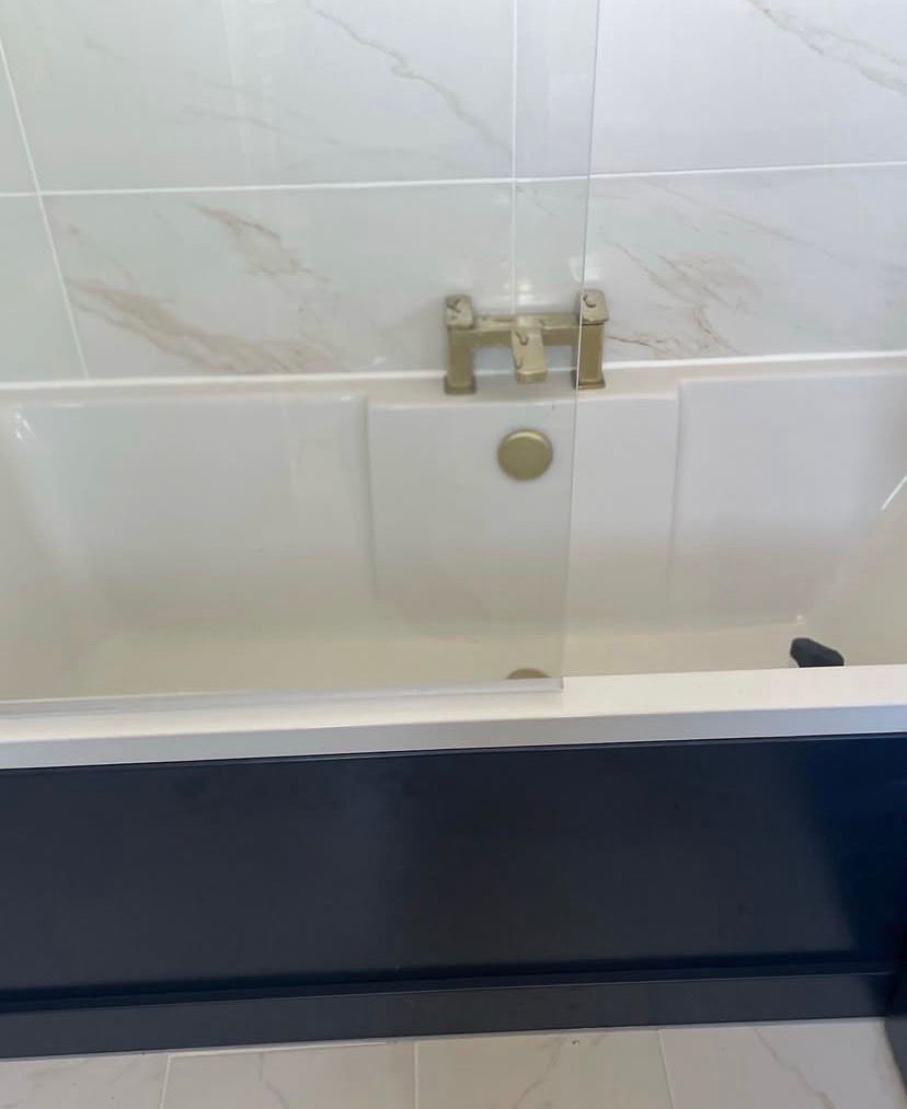Brass bath taps and glass bath screen against marble-effect wall tiling