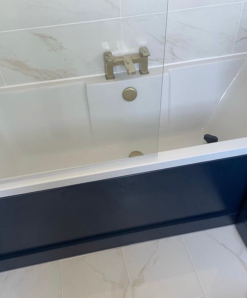 Bath with brass deck-mounted taps, navy bath panel and marble-effect floor tiling