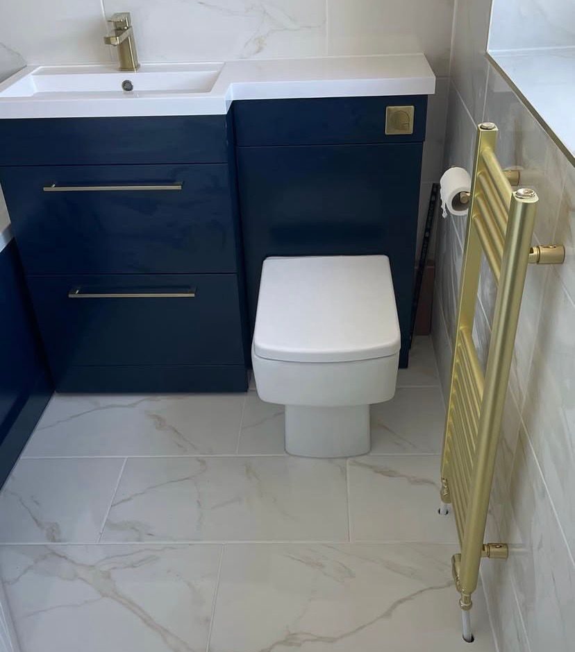 Finished bathroom: navy vanity and WC units, brass towel rail, marble-effect tiling