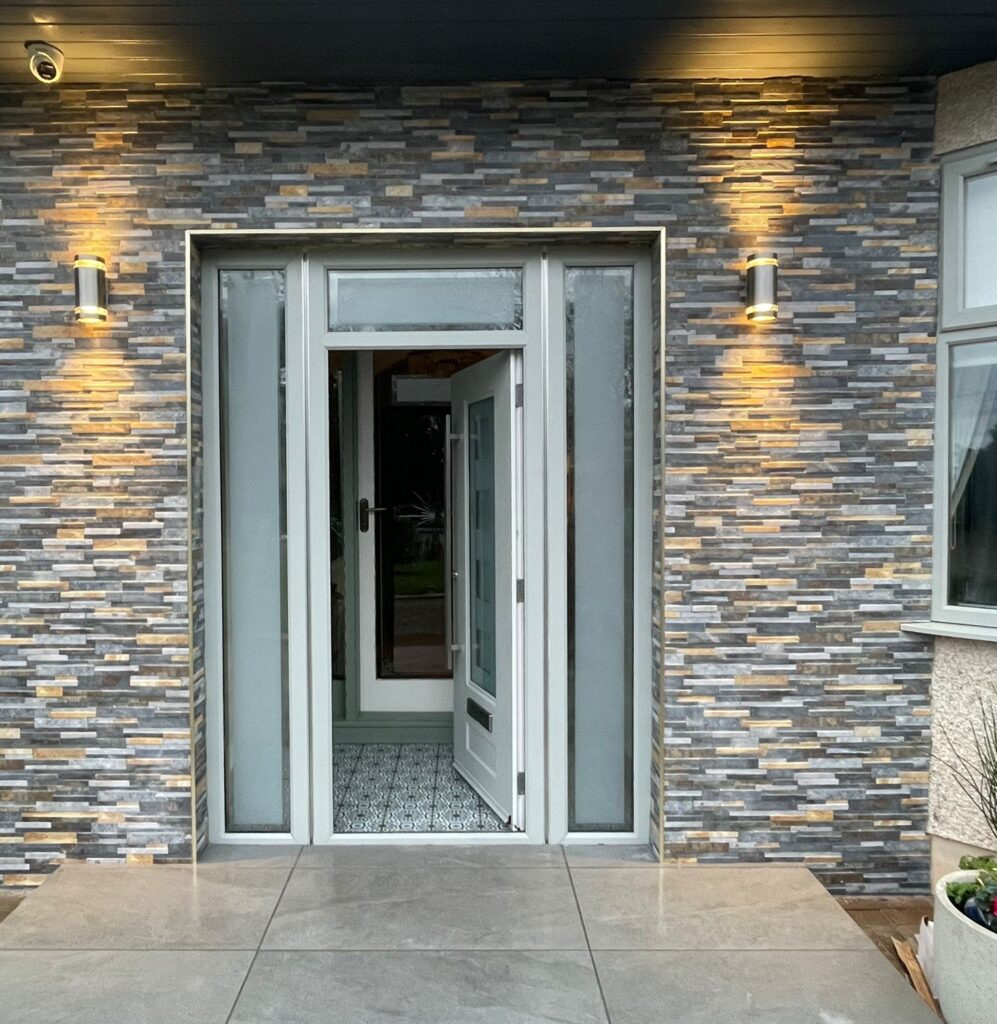 Split-face stone cladding around a porch entrance with porcelain paving and wall lights