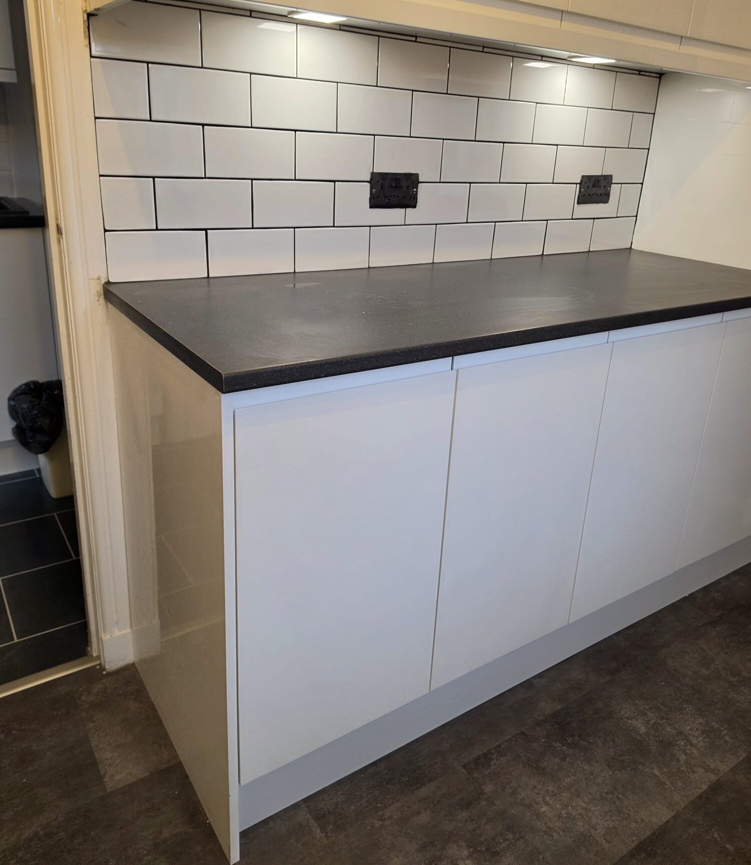 White metro splashback with contrasting dark grout above a black worktop and handleless units